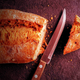 A long loaf of bread with a small piece of the tip sliced off, the knife used to do the job lying nearby.